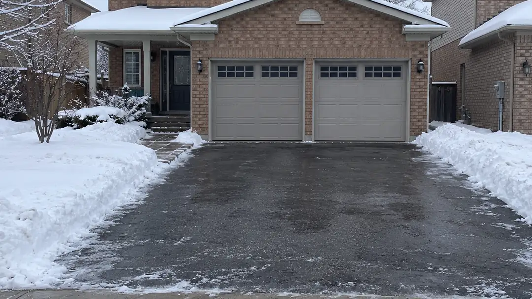 Driveway cleared of snow in front of a brick two-car-garage home, residential snow removal in Milton